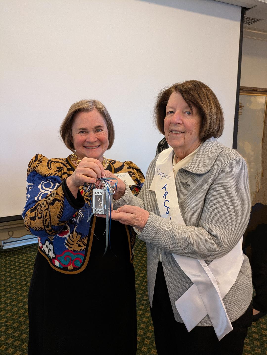 Leslie Petter, ARCS Light 2024 presenting lantern to Sally McDaniel, ARCS Light 2025